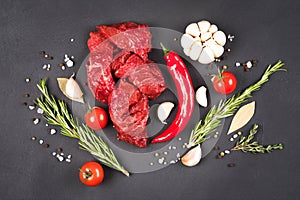 Chopped raw beef or lamb meat with seasonings, chili pepper and vegetables over dark concrete background