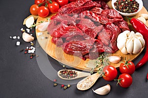 Chopped raw beef or lamb meat with spices, seasoning, chili pepper and tomatoes over dark concrete background