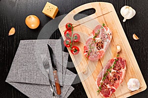 Chopped raw pork steaks with spices, tomatoes and thyme on a cutting kitchen board on a black wooden table. next to a napkin with