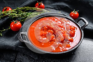 Chopped tinned red tomatoes in a pan. Black background. Top view
