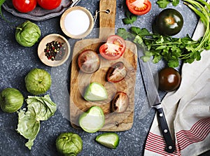 Chopped tomatoes and knife on cutting board, fresh vegetables on the table.