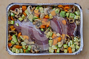 Chopped vegetables: courgettes, yellow tomatoes, onions, as well as mushrooms and meats in a foil container