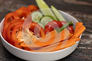 Chopped vegetables, cucumbers, paprika, carrots in a white bowl on wooden table