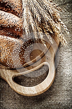 Chopping board bread rye ears on sacking background