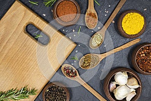Chopping board with free space for text, assortment of spices in wooden utensils on black background