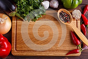 Chopping board, vegetables, herbs and spices in wooden spoon, in