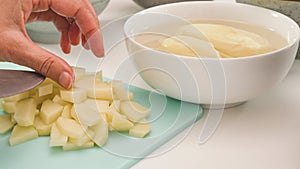 Chopping potatoes on chopping board close up on white kitchen table