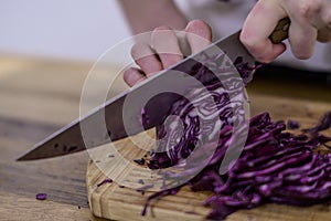 Chopping red cabbage with a kitchen knife on a wooden cutting board