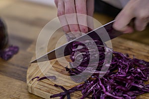 Chopping red cabbage with a kitchen knife on a wooden cutting board