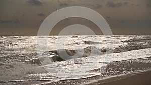 Choppy waves crash on sandy beach under stormy skies. Dramatic seascape shows natures fury. Ocean tempest captured for