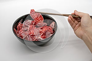 Chopstick holding fresh sliced beef hind shank from black cerami