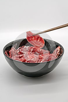 Chopstick holding fresh sliced beef hind shank from black ceramic bowl