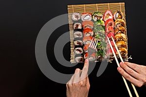 Chopsticks and fork in hand with sushi on black background