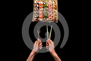 Chopsticks and fork in hand with sushi on black background