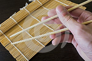 Chopsticks in hand in the background of a bamboo sushi mat