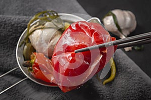 Chopsticks hold fermented red hot peppers against a background of pickled foods.
