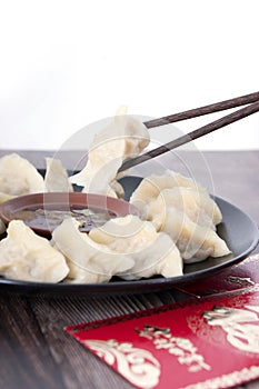 Chopsticks pick up the dumplings on the plate and the red envelopes under the plate.The Chinese meaning in the picture is `happine