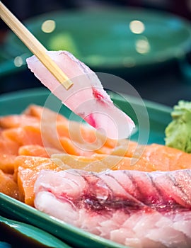 Chopsticks picking a pink sashimi from plate