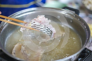 Chopsticks tong slice of fish, dip thin slices of meat in boiling water