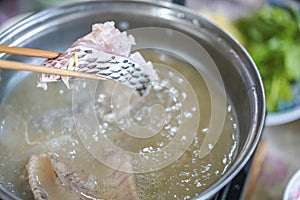 Chopsticks tong slice of fish, dip thin slices of meat in boiling water