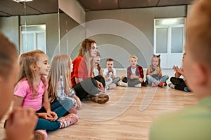 Choreography class. Young female dance teacher sitting on the floor with group of happy children in the dance studio