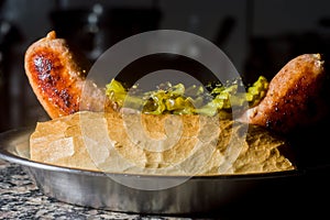 choripan, bread with sausage and pickles on a plate with dark background and copy space