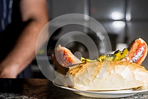 choripan, bread with sausage and pickles on a plate with dark background and copy space