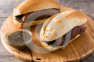 Choripan. Traditional Argentina sandwich with chorizo and chimichurri sauce on wooden table