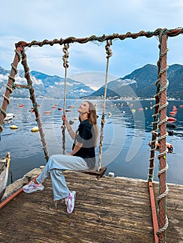 Chraming woman sits on the swing and smiles at the sea shore