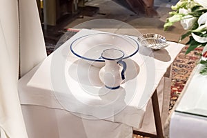 Christening objects prepared on a table inside a church. Jug with blessed water, basin and shell.