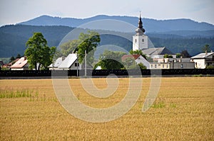 Christian church as an part of village, forested hills in background, yellow field of grain in foreground