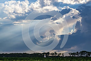 Christian church in the field lit by the rays of the sun breaking through the rain clouds