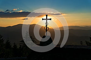 Christian cross against sunset and hills on the background