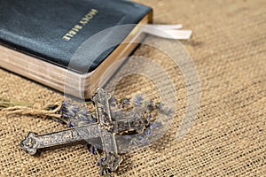 Christian cross on lavanda flowers next to Holy Bible