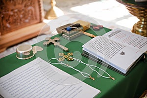 Christian cross, an open  Bible with the text of a prayer, bottles of oil on a table with a green tablecloth in an Orthodox Church