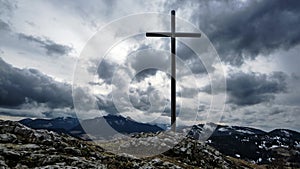 Christian cross on a rock in a mountain landscape, Dramatic clouds over the silhouette of the mountains in winter