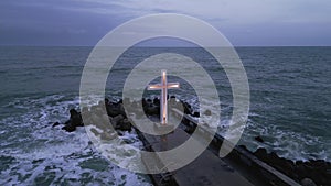 christian cross standing on pier in the sea or ocean with dramatic sky at night