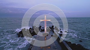 christian cross standing on pier in the sea or ocean with dramatic sky at night