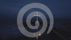 christian cross standing on pier in the sea or ocean with dramatic sky at night