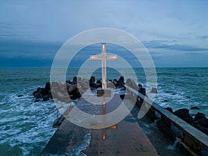 christian cross standing on pier in the sea or ocean with dramatic sky at night