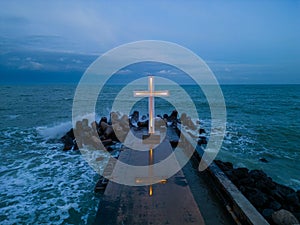 christian cross standing on pier in the sea or ocean with dramatic sky at night