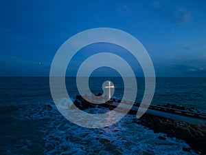 christian cross standing on pier in the sea or ocean with dramatic sky at night