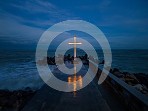 christian cross standing on pier in the sea or ocean with dramatic sky at night