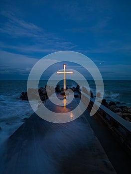 christian cross standing on pier in the sea or ocean with dramatic sky at night