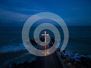 christian cross standing on pier in the sea or ocean with dramatic sky at night