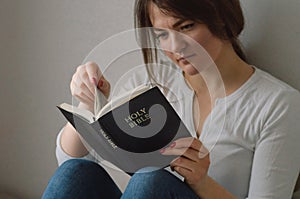 Christian girl holds bible in her hands. Reading bible in a the living room. Concept for faith, spirituality and religion