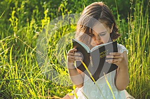 Christian girl holds bible in her hands. Reading the Holy Bible in a field during beautiful sunset. Concept for faith