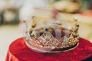 Christian golden crown for holy matrimony on red table in church. Wedding spiritual ceremony. Golden crown with red and blue