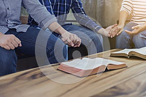 A christian group holding hands and together over blurred bible on wooden table, fellowship or bible study concept