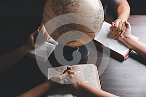 Christian group praying for globe and people around the world on wooden table with bible. Christian small group holding hands and